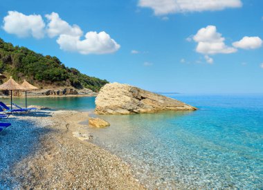 Yaz sabah Pulebardha plaj şezlong, strawy şemsiye ve çakıl (Saranda, Arnavutluk).