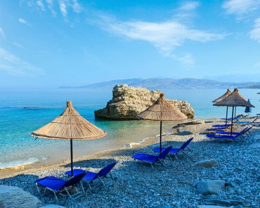 Yaz sabah Pulebardha plaj şezlong, strawy şemsiye ve çakıl (Saranda, Arnavutluk).