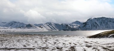 İzlanda dağlarında mevsim değişimi. Sonbaharda kar altında renkli Landmannalaugar dağları. Dağın eteğindeki Frostastadavatn Gölü.