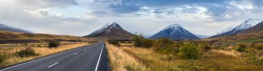 İzlanda 'da otomobil gezisi sırasında otoyol ve dağ manzarası. Manzaralı İzlanda manzarası: fiyortlar, tarlalar, bulutlar, buzullar, şelaleler.