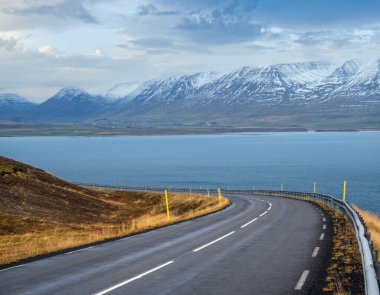 İzlanda 'da otomobil gezisi sırasında otoyol ve dağ manzarası. Manzaralı İzlanda manzarası: fiyortlar, tarlalar, bulutlar, buzullar, şelaleler.