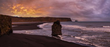 Reynisfjara Okyanusu 'nun siyah volkanik kumsal sahili ve Dyrholaey Burnu, Vik, Güney İzlanda' dan kaya oluşumları. Arkaplanda Reynisfjall Dağı.