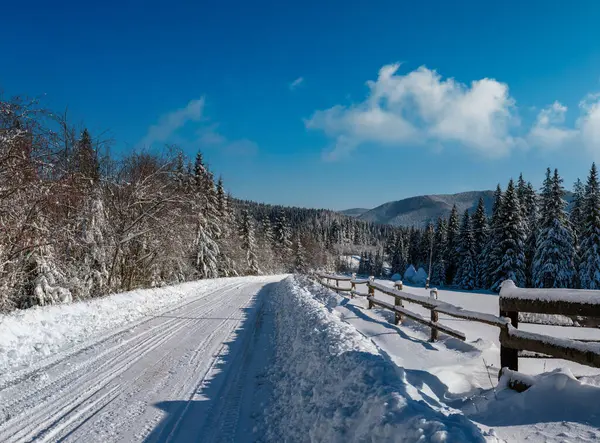 通过雪地冷杉林 雪地漂移和路边木栅栏通往偏远山区村落的二级乡村高山道路 — 图库照片