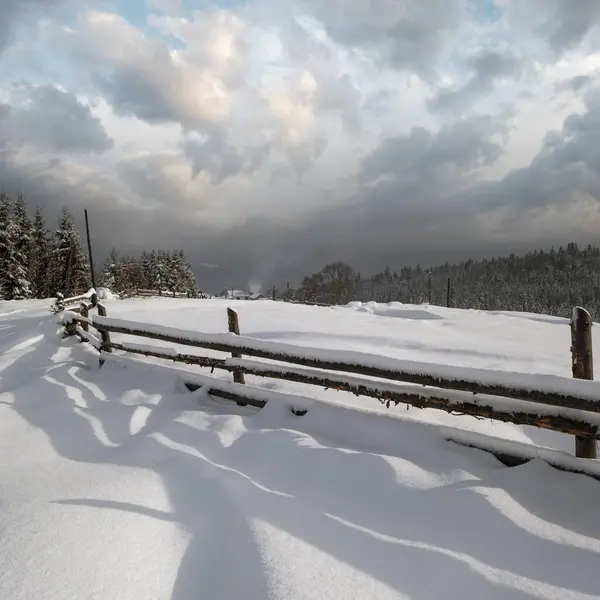 风景如画的影子在雪地上从木栅栏上飘扬 高山冬季小村子郊外 雪地小径 长满了冷杉 长满了薄雾 多云的小山 — 图库照片