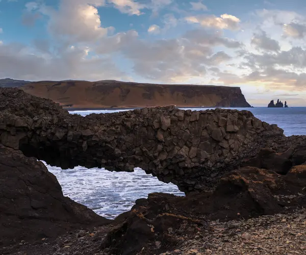 Reynisfjara Okyanusu 'nun siyah volkanik kumsal sahili ve Dyrholaey Burnu, Vik, Güney İzlanda' dan kaya oluşumları. Arkaplanda Reynisfjall Dağı.