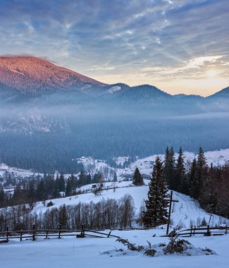 Sunrise sabah kış dağ köyü ilçe sınırı siyah Çeremoş Nehri Vadisi alp arasında. Kırsal karla kaplı yolu görünümünden Hıristiyanlık ile tepenin yamacında haçlar, Zelene, Verkhovyna, Ukrayna.