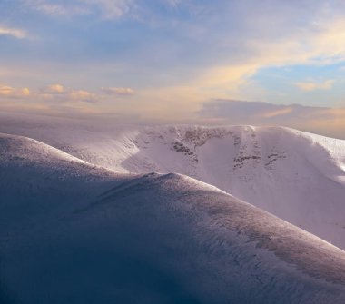 Kar dün akşam güneş ışığında kış dağlarını kapladı. Resimli alp kayak merkezinin tepesinde muhteşem rüzgarlı bir alacakaranlık.