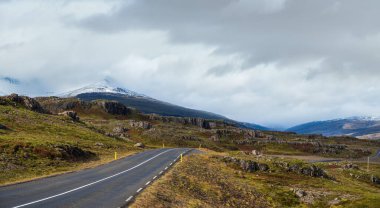 İzlanda 'da otomobil gezisi sırasında otoyol ve dağ manzarası. Manzaralı İzlanda manzarası: fiyortlar, tarlalar, bulutlar, buzullar, şelaleler.