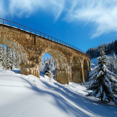 Demiryolu üzerindeki taş viyadük (kemer köprüsü) dağ karlı köknar ormanı boyunca. Karlar yol kenarına sürükleniyor ve ağaçlar ve elektrik kabloları üzerindeki buzlar eriyor..