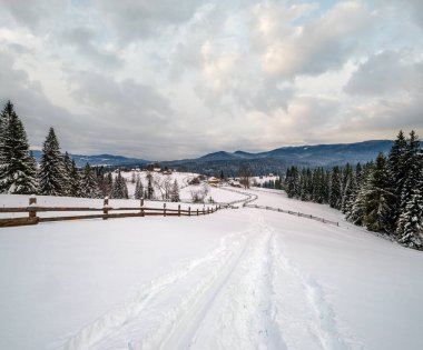 Uzak dağ köyündeki ikincil kırsal dağ yolu, yol kenarındaki karlar ve ahşap çitler.