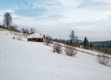 Kırsal tepeler, koruluklar ve tarım arazileri uzak kışın uzak dağlık dağ köyü ve tepede terk edilmiş küçük eski bir ev.