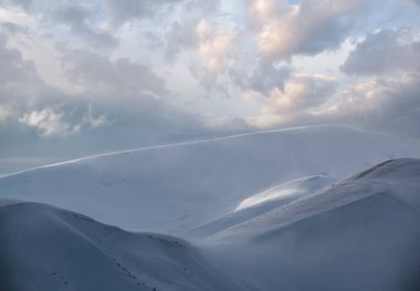 Kar dün akşam güneş ışığında kış dağlarını kapladı. Resimli alp kayak merkezinin tepesinde muhteşem rüzgarlı bir alacakaranlık.