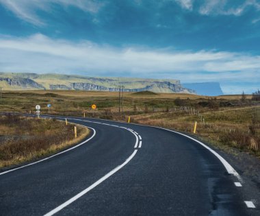 İzlanda 'da otomobil gezisi sırasında otoyol ve dağ manzarası. Manzaralı İzlanda manzarası: fiyortlar, tarlalar, bulutlar, buzullar, şelaleler.