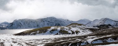 İzlanda dağlarında mevsim değişimi. Sonbaharda kar altında renkli Landmannalaugar dağları. Dağın eteğindeki Frostastadavatn Gölü.
