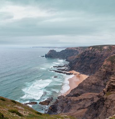 Sandy beach taşlı sırtlar ile hava görünümü yaz Atlantik kayalık kenarı (Costa Vicentina, Algarve, Portekiz) bulutlu. Ve okyanus sörf dalgalar.