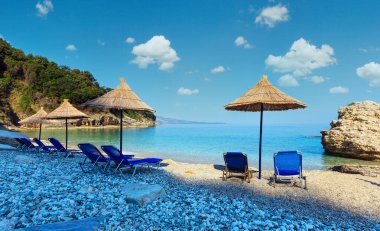 Yaz sabah Pulebardha plaj şezlong, strawy şemsiye ve çakıl (Saranda, Arnavutluk).