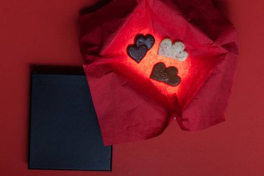 Heart shaped chocolates inside of a glowing box with a red background and a black lid for text