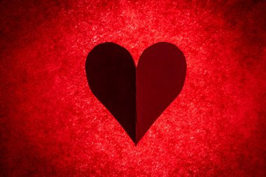 Hand cut of a heart on a bright red back lite background