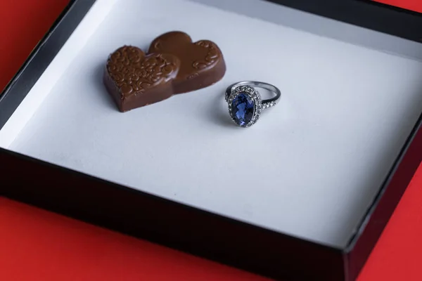 赤の背景に白い箱の中にチョコレートとブルーサファイアリング — ストック写真
