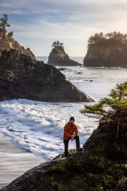 Man sitting on a rock enjoying the amazing view of the sea and sea stacks in this beautiful spot on the Oregon coast