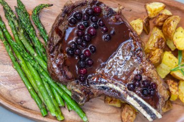 Pirzola ile ızgara kemik. Patates ve asparragus ile servis ediliyor. Taze yaban mersini limanı redüksiyonu da var.