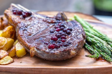 Pirzola ile ızgara kemik. Patates ve asparragus ile servis ediliyor. Taze yaban mersini limanı redüksiyonu da var.