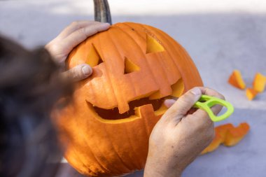 Eller havada gülümseyen bir balkabağı oyuyor ve masanın üzerinde parçalar var.