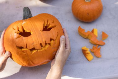Eller açık havada oyulmuş bir balkabağı tutuyor ve masada parçalar var.