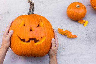 Eller açık havada oyulmuş bir balkabağı tutuyor ve masada parçalar var.
