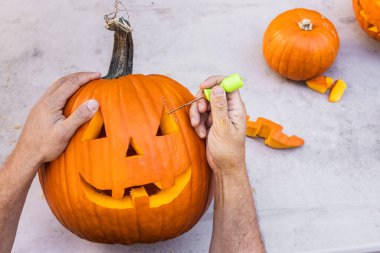 Eller havada gülümseyen bir balkabağı oyuyor ve masanın üzerinde parçalar var.