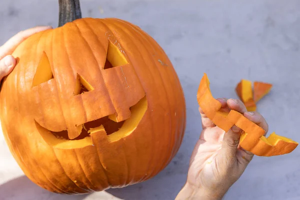 Hands holding a carved pumpkin outdoors with pieces on the table