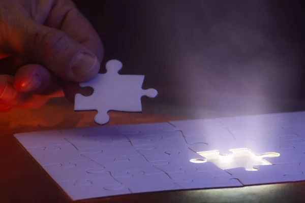 close up of a hand holding the missing puzzle piece with a glow showing where the piece goes and a bit of mist in the air.