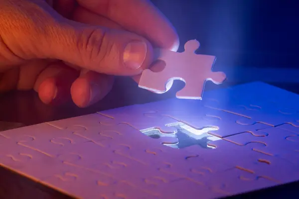 close up of a hand holding the missing puzzle piece with a glow showing where the piece goes and a bit of mist in the air.