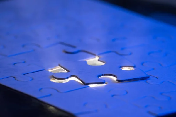 close up of a blank puzzle with a blue light and a beam of light from underneath as a concept.