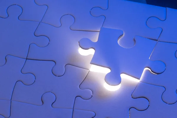close up of a blank puzzle with a blue light and a beam of light from underneath as a concept.