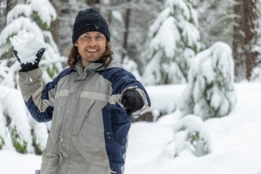 Gri ve mavi ceketli bir adam elinde bir kar topu tutuyor. Gülümsüyor ve karın tadını çıkarıyor.