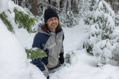 Siyah şapkalı bir adam karın üzerinde duruyor. Gülümsüyor ve kameraya bakıyor.