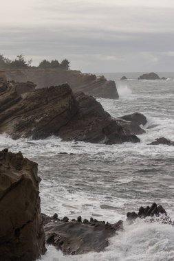 Arka planda büyük bir su kütlesi olan kayalık bir kıyı şeridi. Dalgalar kayalara çarpıyor, güçlü ve dinamik bir sahne yaratıyor. Sahne dayanıklılık ve dayanıklılıktan oluşur.