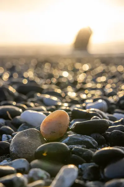 A small rock is sitting on a beach with a large rock in the background. The rock is surrounded by many other rocks, creating a rocky and rugged landscape. Concept of solitude and tranquility