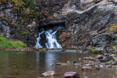 Kayalık bir kıyı şeridi olan bir şelale nehre akıyor. Su sakin ve berrak ve kayalar tüm bölgeye dağılmış durumda. Sahne huzurlu ve sakin, suyun sesiyle.