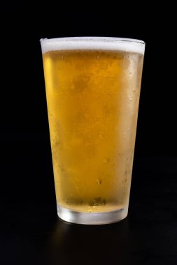 Masanın üzerinde bir bardak bira duruyor. Bardağın yarısı dolu ve biralar köpüklü.