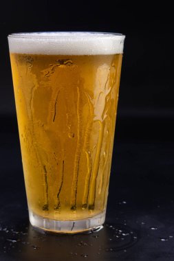 Bir bardak bira, üzerinde buhar olan bir masanın üzerinde duruyor. Bardağın yarısı dolu ve buharlaşma yan taraftan damlıyor. Rahatlama ve keyif kavramı