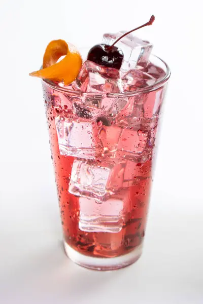 A glass of pink drink with a cherry on top. The drink is cold and refreshing. The cherry adds a pop of color and a touch of sweetness to the drink. The glass is filled with ice