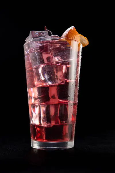 A glass of pink drink with ice cubes and an orange slice on top. The drink appears to be a cocktail
