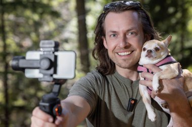 Adam kendini ve elinde tuttuğu bir chihuahua 'yı kameraya çekmek için telefon zili kullanıyor. Film doğal bir orman bölgesinde çekiliyor..