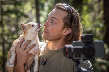 Adam kendini ve elinde tuttuğu bir chihuahua 'yı kameraya çekmek için telefon zili kullanıyor. Film doğal bir orman bölgesinde çekiliyor..