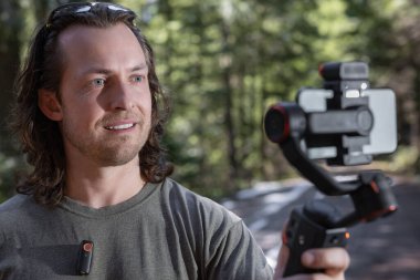 İçerik yaratıcısı kullanıyor. Arka planda bulanık bir orman olan doğada çekilecek bir telefon dinamiği.