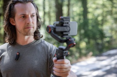 İçerik yaratıcısı kullanıyor. Arka planda bulanık bir orman olan doğada çekilecek bir telefon dinamiği.