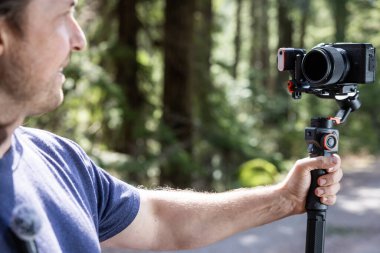 İçerik yaratıcısı, arka planda bulanık bir orman ile doğayı filme almak için bir kamera telsizi kullanıyor.
