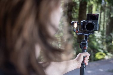 İçerik yaratıcısı, arka planda bulanık bir orman ile doğayı filme almak için bir kamera telsizi kullanıyor.